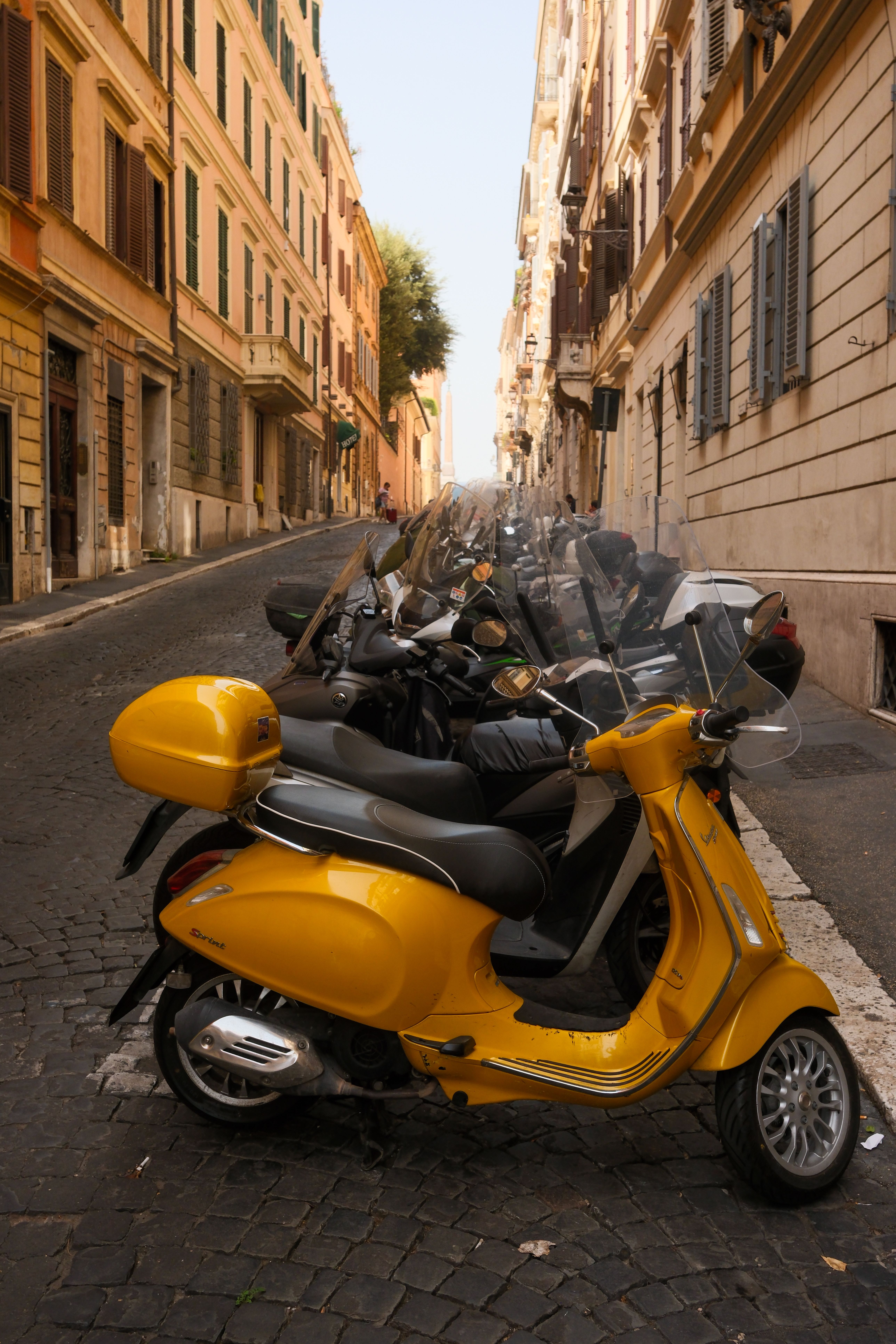 Vibrant yellow scooter parked along a picturesque Italian street lined with classic architecture.