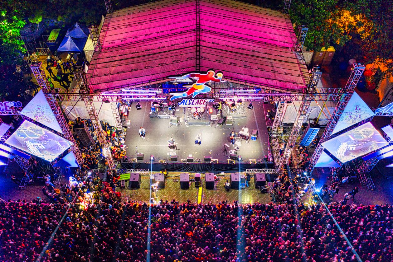 Aerial night view of a large outdoor concert crowd with colourful stage lighting at a music festival