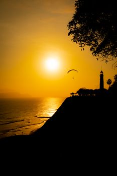 Dramatic silhouette of a lighthouse during an orange sunset over the Pacific Ocean in Lima, Peru.