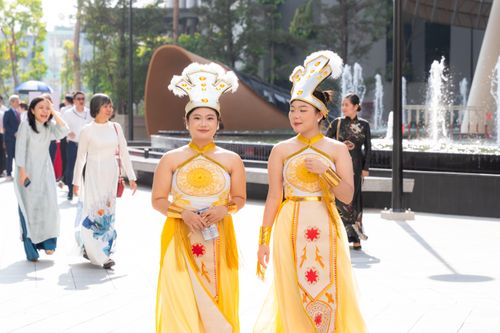 Free Women in traditional yellow attire walk through an urban setting, blending culture with modern city life. Stock Photo