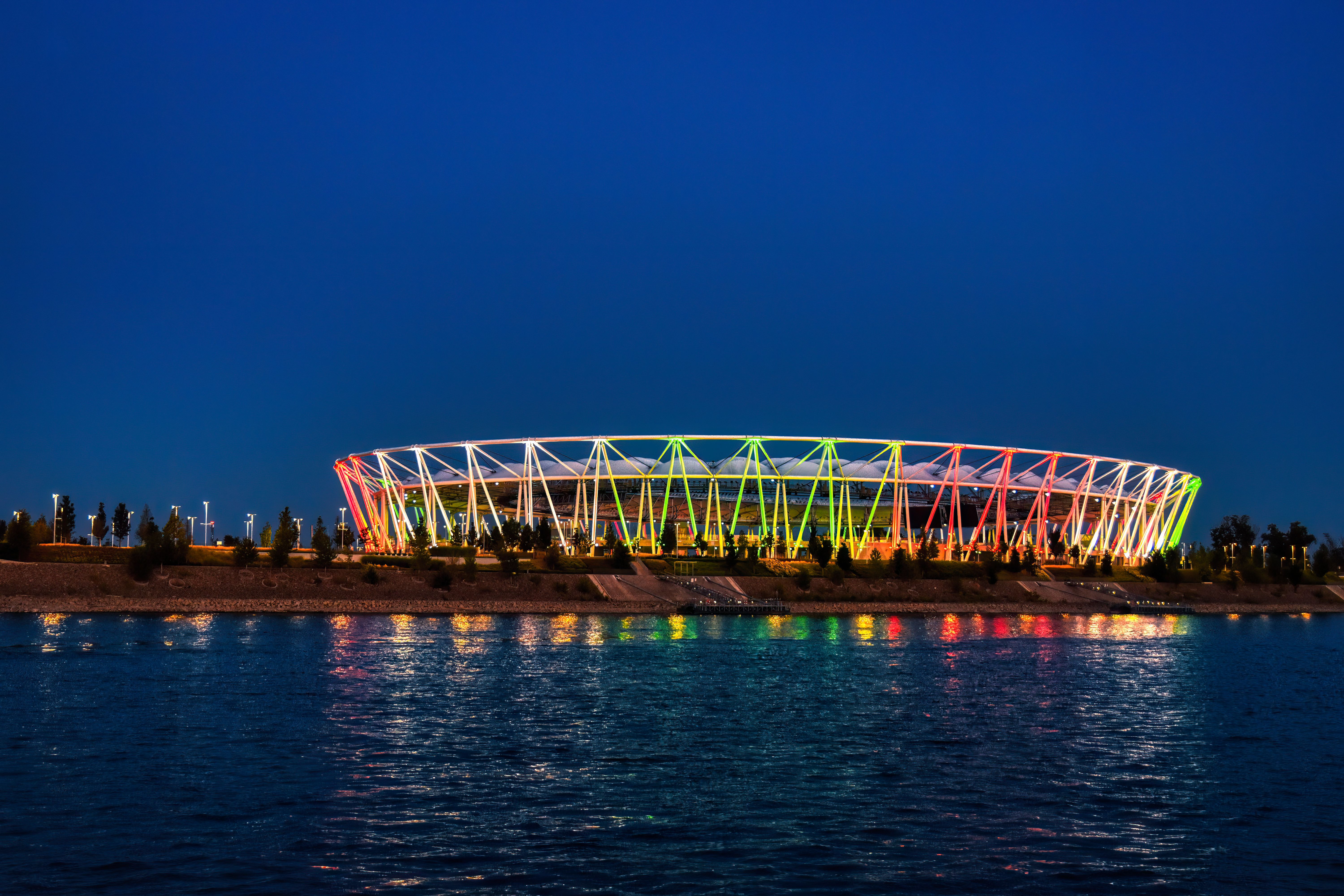 Colorful lights illuminate the stadium in Budapest, Hungary, reflecting on the river at night.