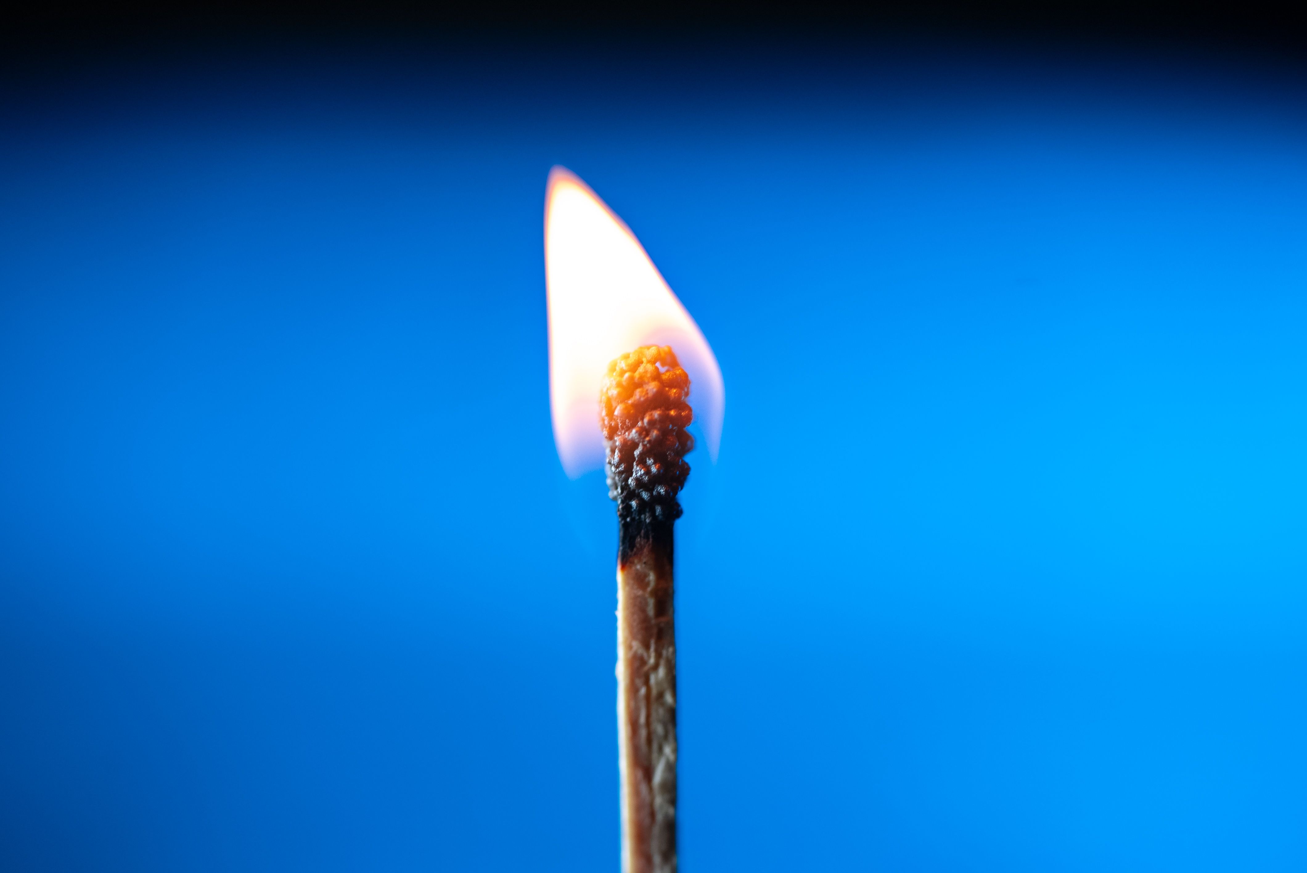 A close-up image of a single matchstick burning, casting a warm glow against a blue background.
