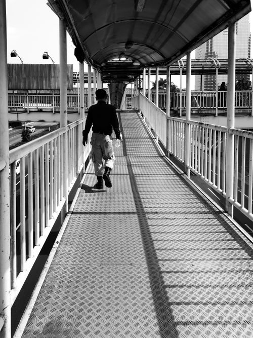 Free Black and white image of a man walking on a pedestrian bridge in Jakarta, Indonesia. Stock Photo
