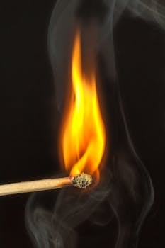 Photo by Pixabay A detailed view of a matchstick burning with bright flame against a dark background, emitting smoke.