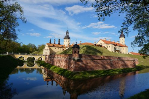 Free Stunning view of the historic Nesvizh Castle with reflections in the surrounding moat under a bright blue sky. Stock Photo