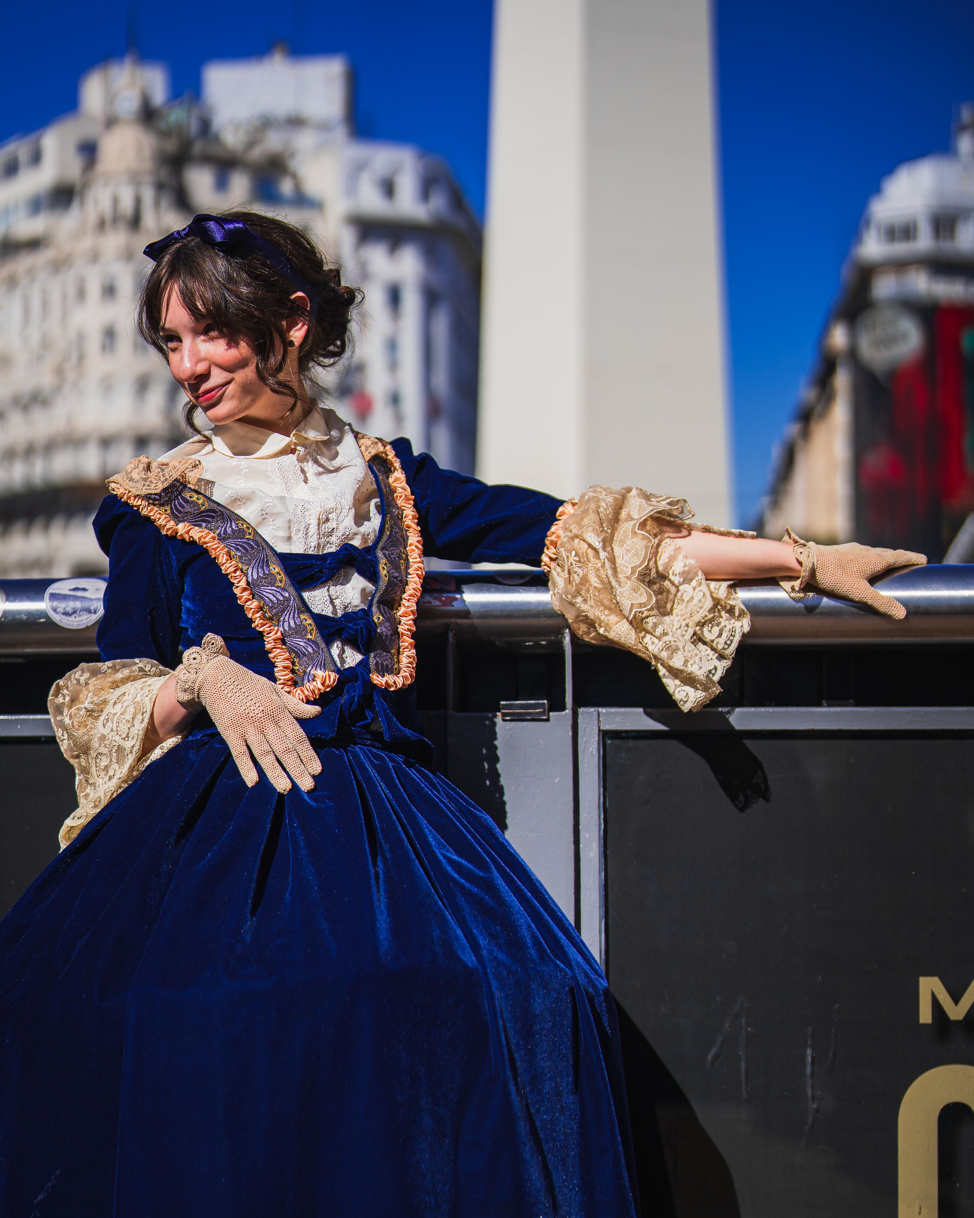 Woman in period costume posing elegantly near an iconic tall structure.
