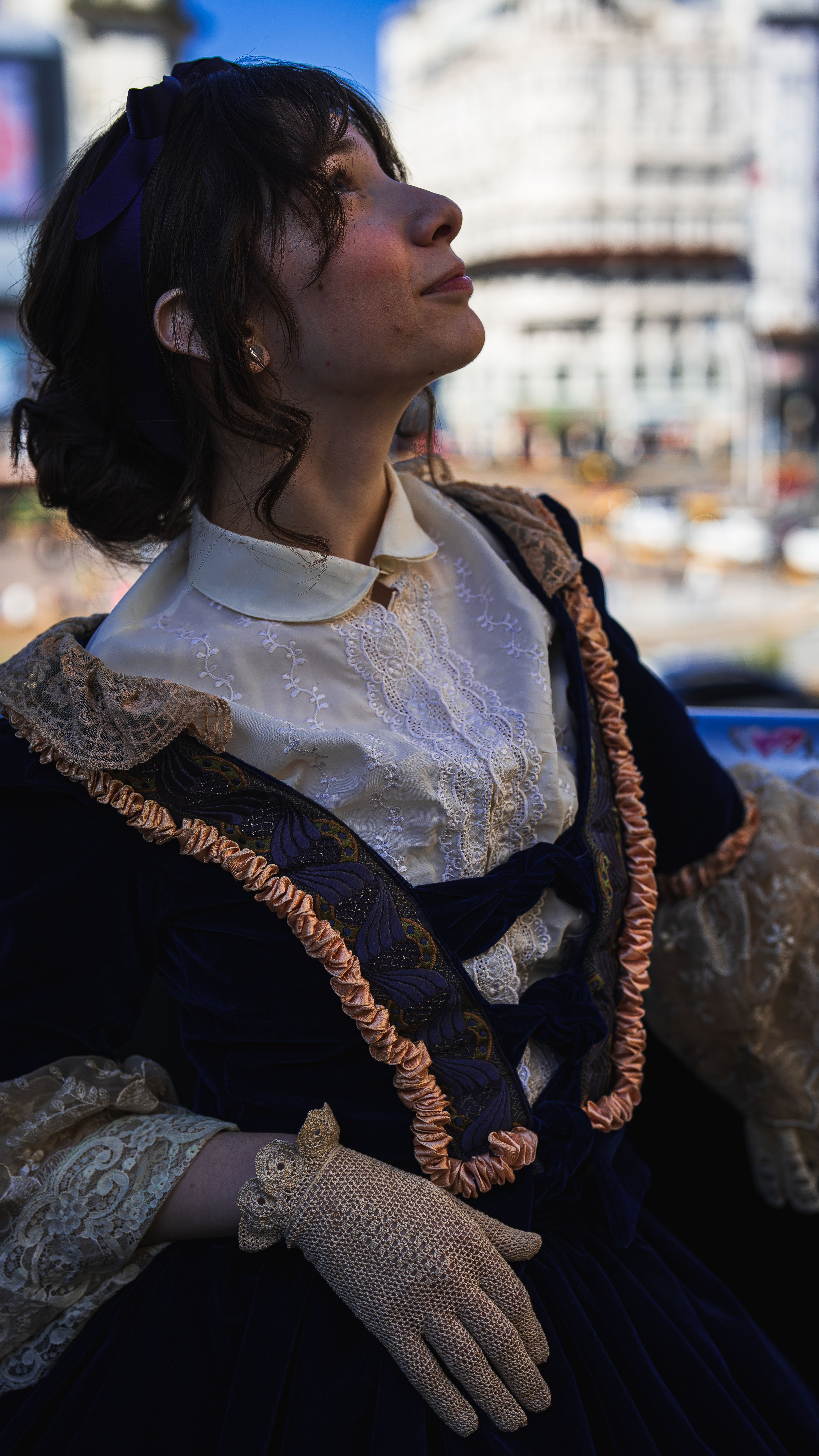 Elegant woman in vintage lace dress, sunlit outdoors. Timeless fashion captured in urban setting.