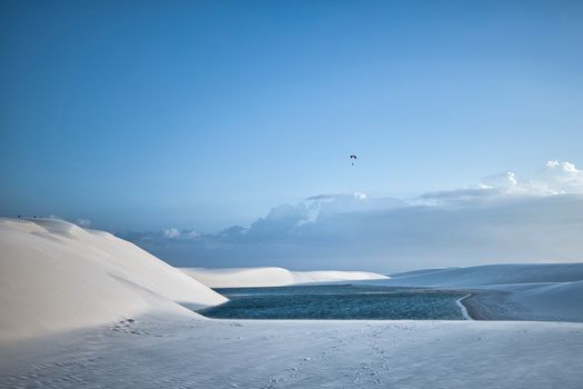 Captured the expansive white dunes and clear lagoon of Lençóis Maranhenses, Brasil, under a bright blue sky.