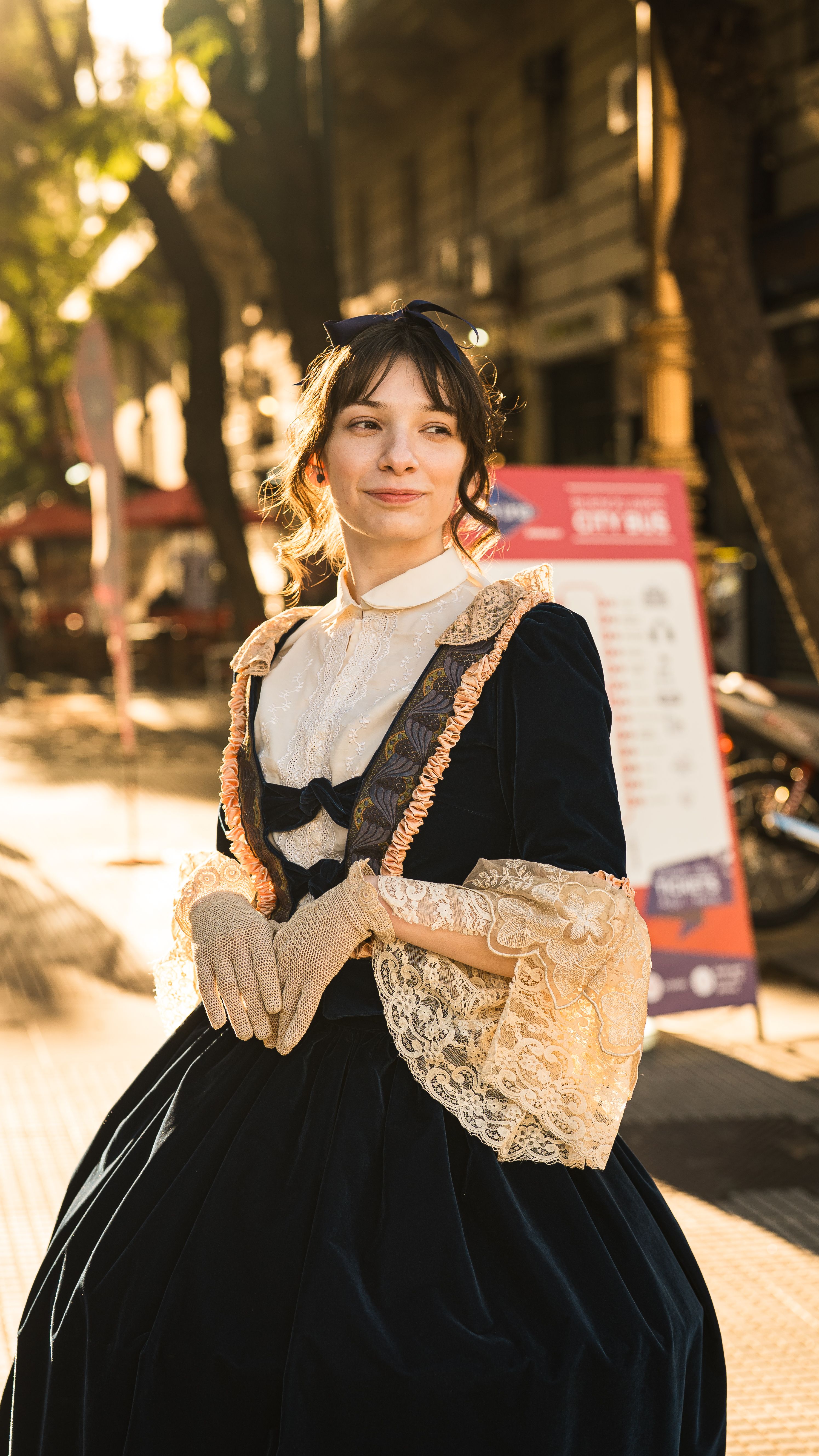 A woman in Victorian attire standing outdoors in sunlight, exuding elegance.