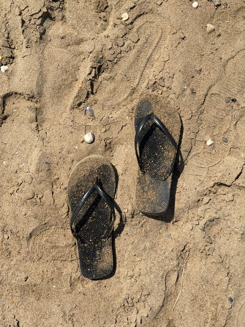 Free A pair of black flip flops on a sandy beach in Antalya, Türkiye, under bright daylight. Stock Photo