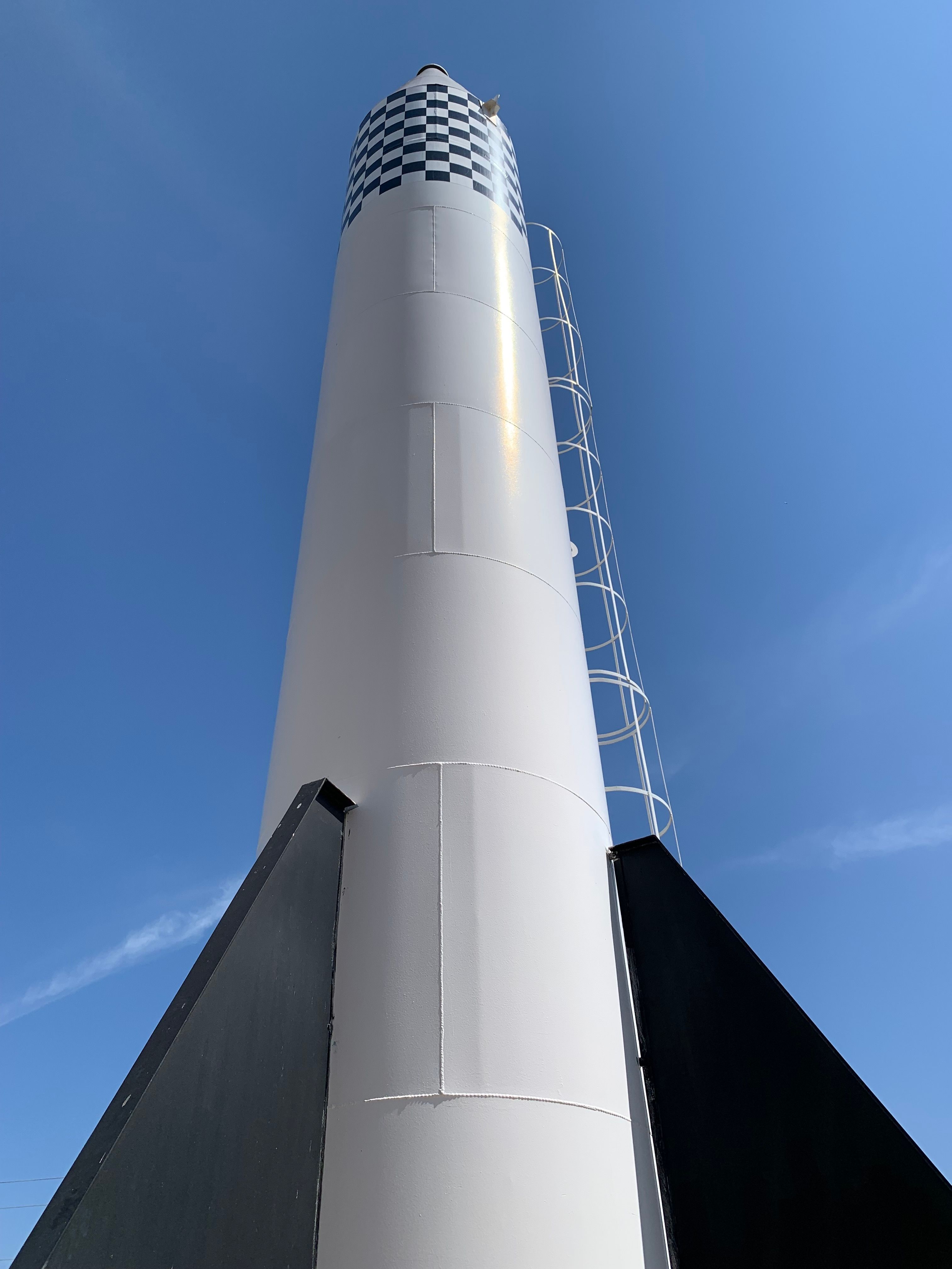 Upward view of a large rocket monument in Varginha, MG, under a clear blue sky.
