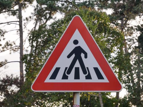 Free A triangular pedestrian crossing sign with trees in the background, indicating caution for drivers. Stock Photo