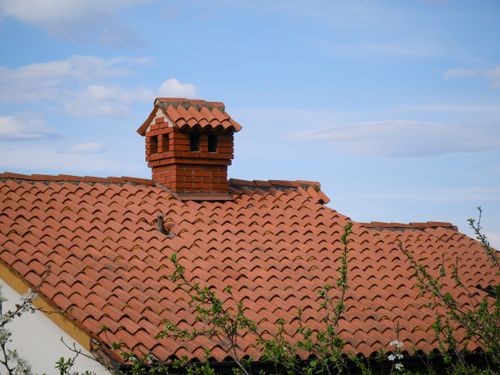 Free A charming red brick chimney stands atop a detailed clay-tiled roof under a clear blue sky. Stock Photo