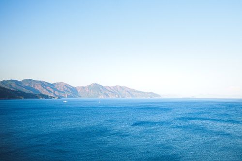 Free Peaceful blue ocean and distant mountain range under a clear sky, perfect for relaxation imagery. Stock Photo