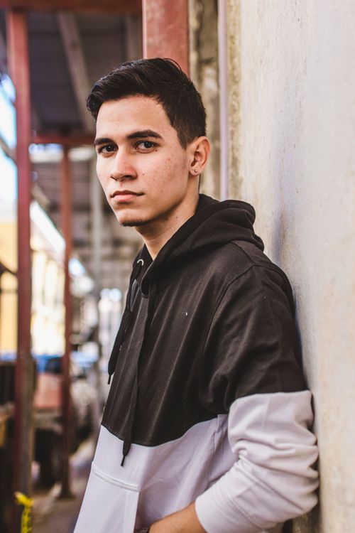 Free A young man in a hoodie leans against a wall in an urban environment, gazing confidently. Stock Photo