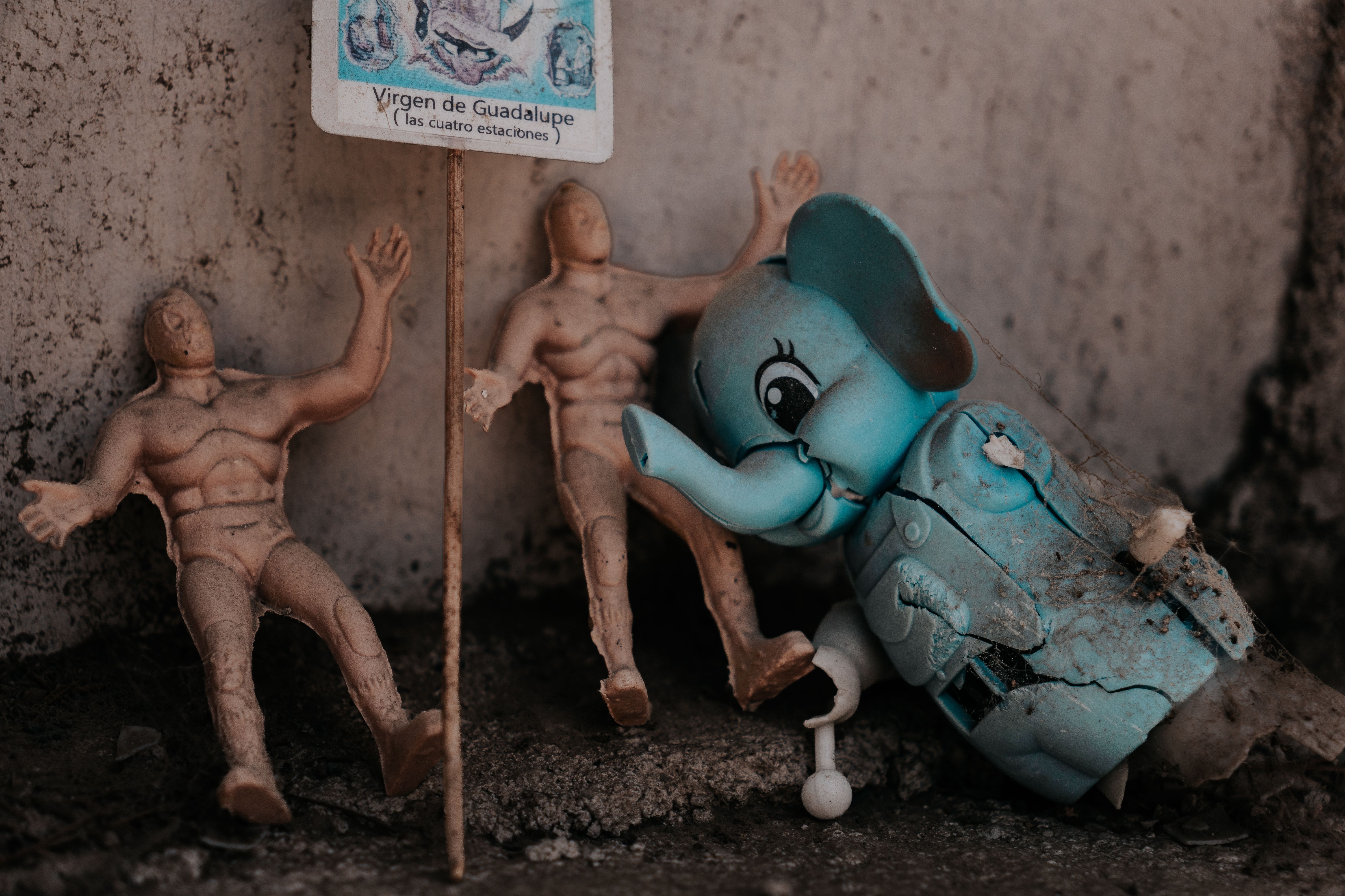 A collection of vintage toys and figurines, with Virgen de Guadalupe sign, in a dusty corner.