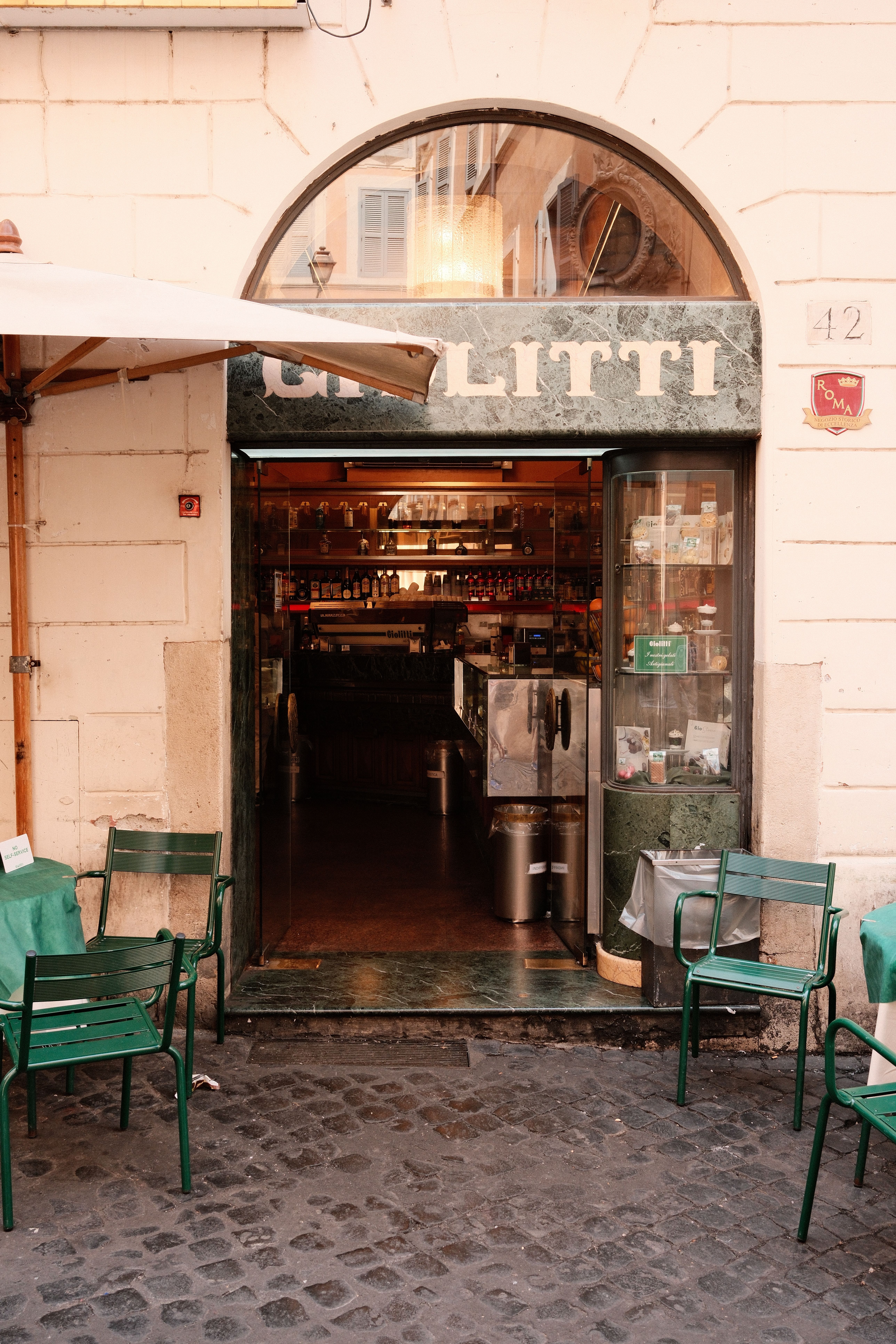 Charming café entrance with green chairs on a cobblestone street.