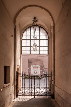 Softly lit corridor with an ornate gate and arch, leading to an exterior view, evokes a classic architectural charm.