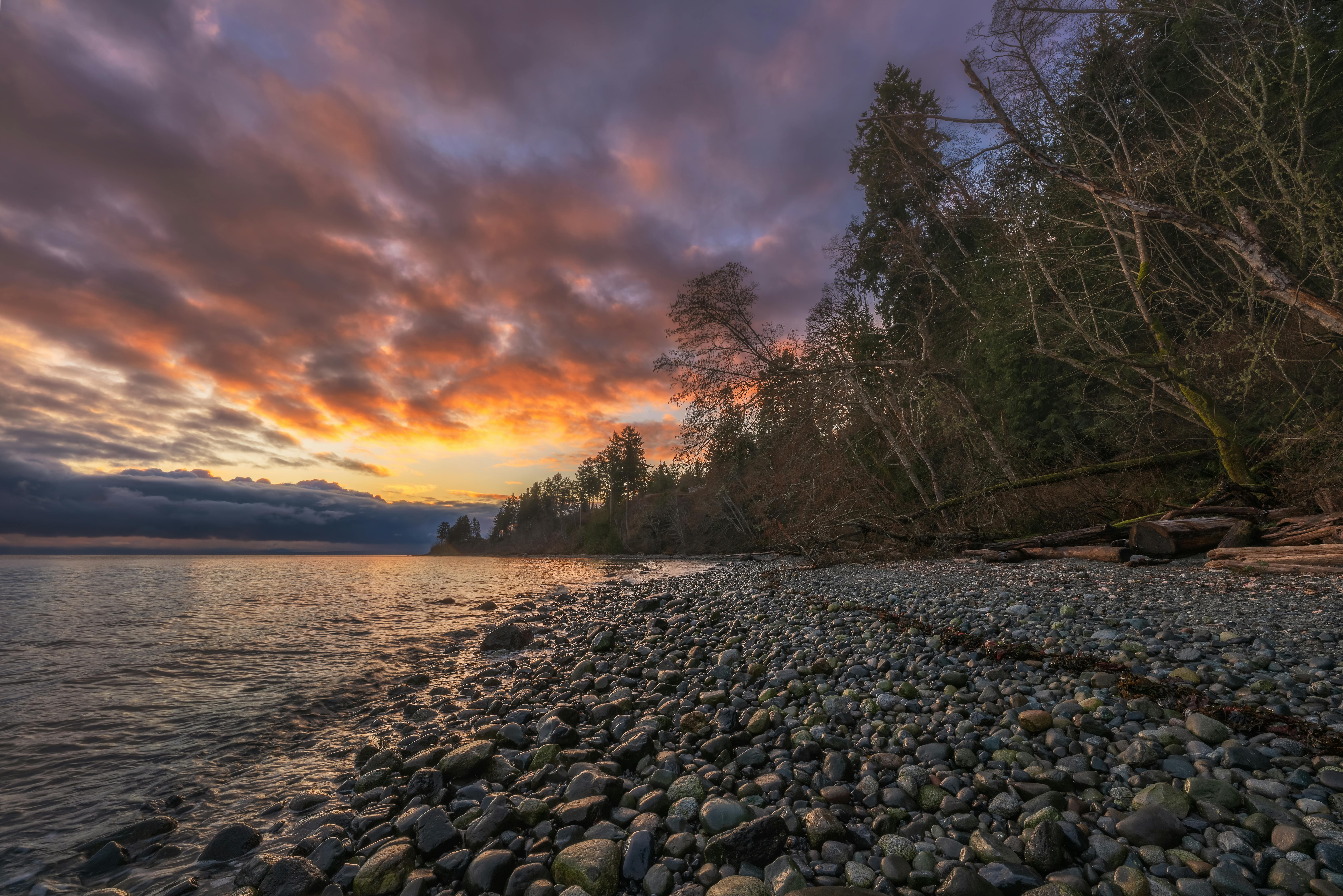 Stunning sunset over a tranquil pebble beach in Courtenay, BC, Canada, with vibrant sky and peaceful waters.