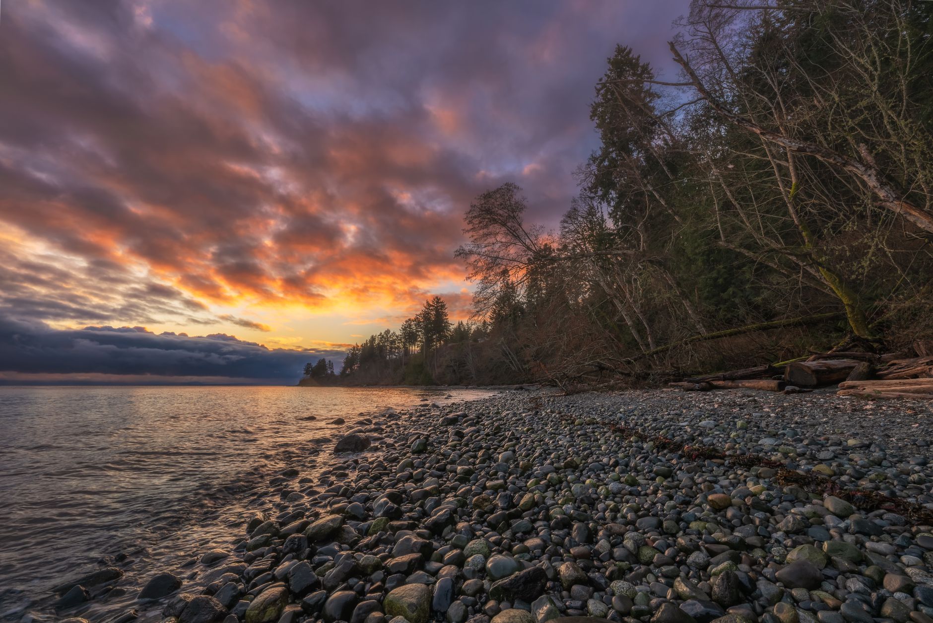 Stunning sunset over a tranquil pebble beach in Courtenay, BC, Canada, with vibrant sky and peaceful waters.