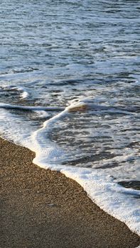 Gentle ocean wave caressing a sandy beach at sunrise, capturing tranquility and nature's beauty.