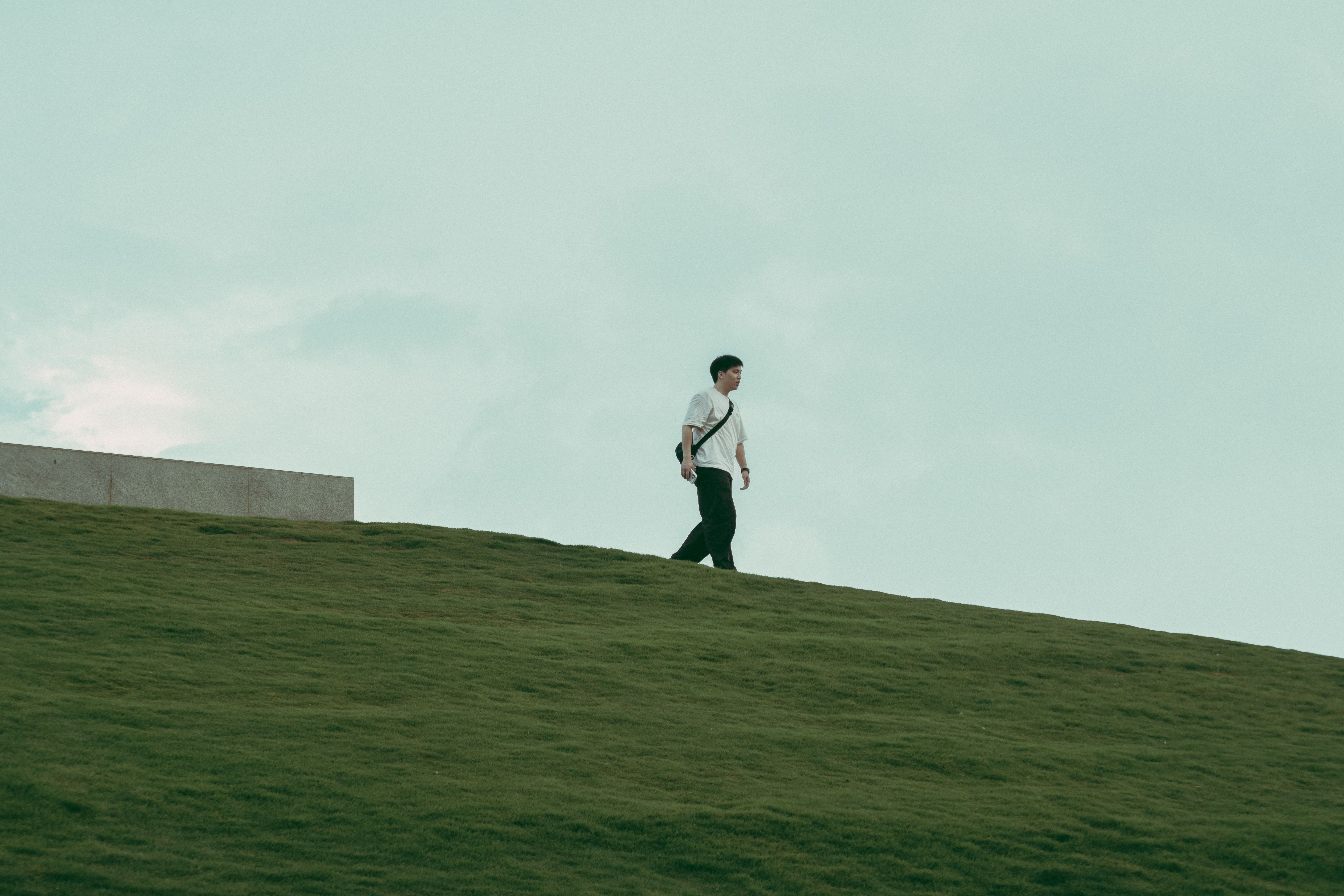 A person walks alone on a grassy hill under a cloudy sky, evoking solitude and tranquility.