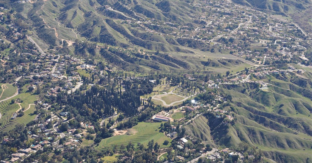 An aerial photograph showcasing rolling hills, suburban houses, and lush greenery.