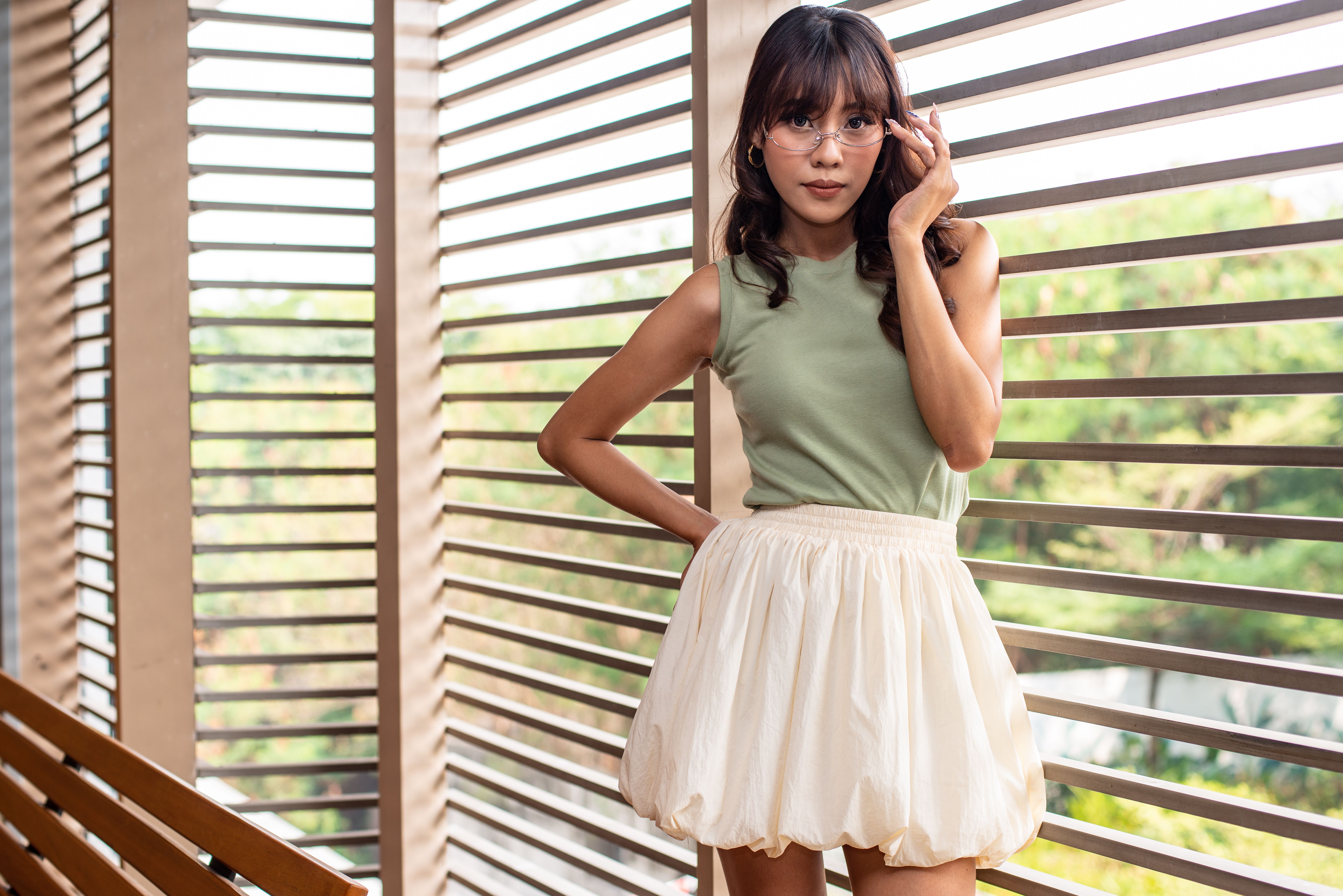 Young woman in fashionable attire poses against contemporary slatted background indoors.