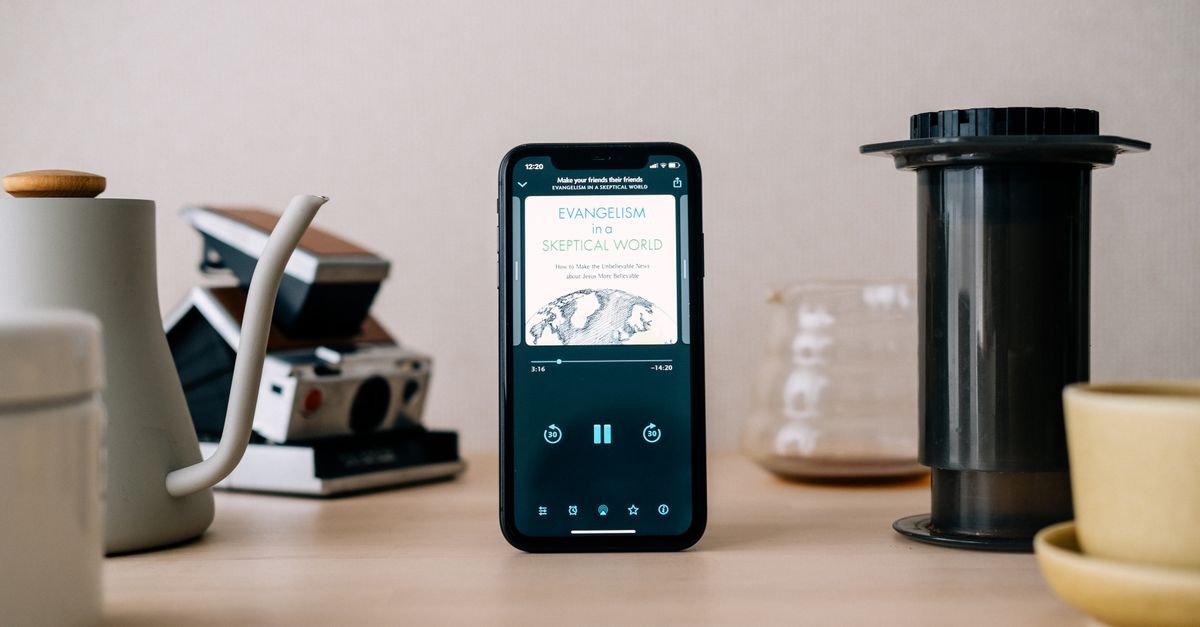 Smartphone exibindo conteúdo cercado por equipamentos de preparo de café em uma mesa de madeira. Configuração minimalista e moderna.
