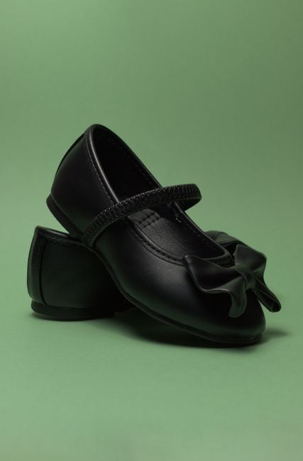 Fotomural Un par de elegantes zapatos negros de niña con lazos, expuestos sobre una superficie verde.