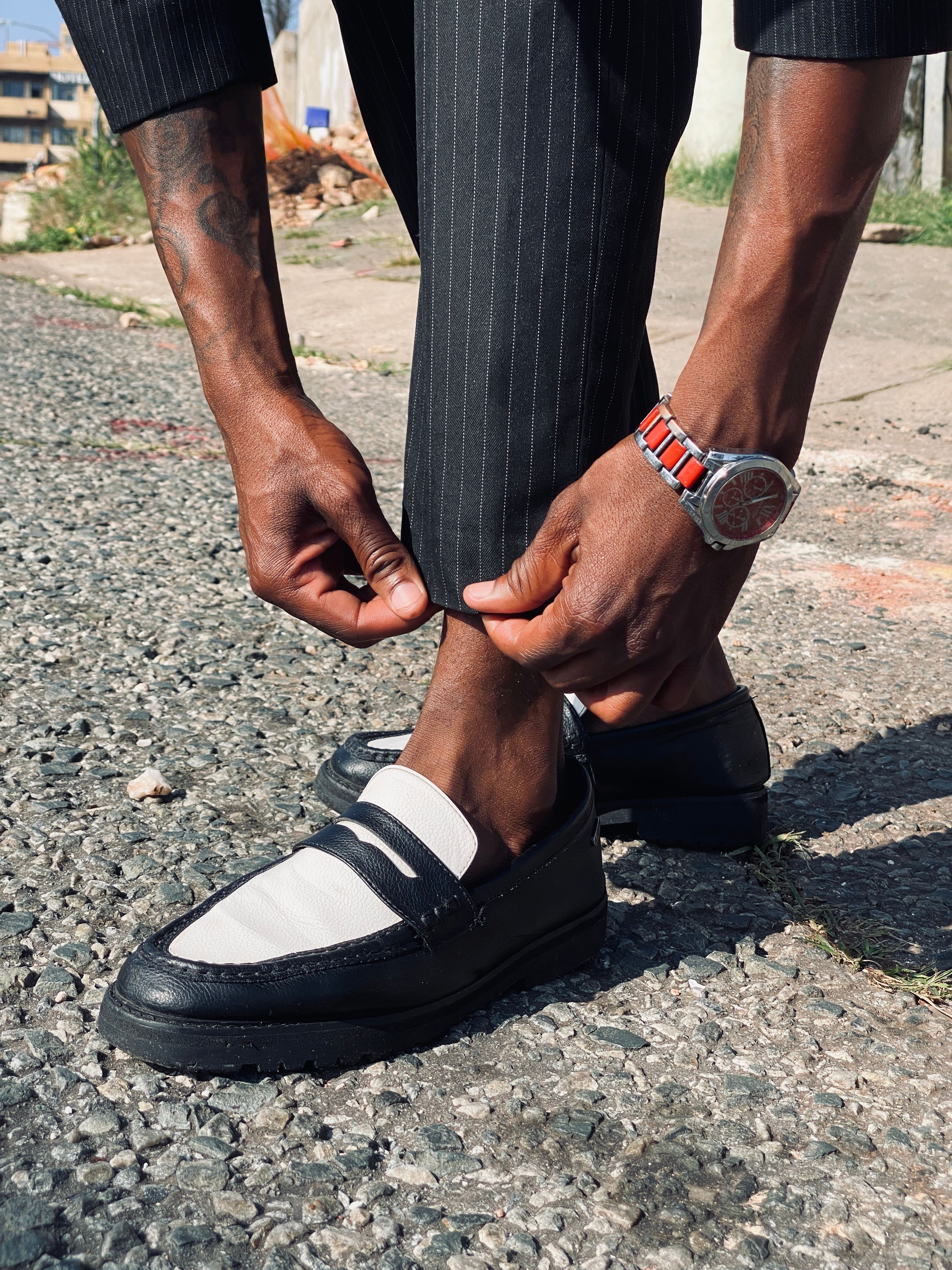A fashionable man adjusts his suit pants, showcasing stylish loafers on a sunny day.