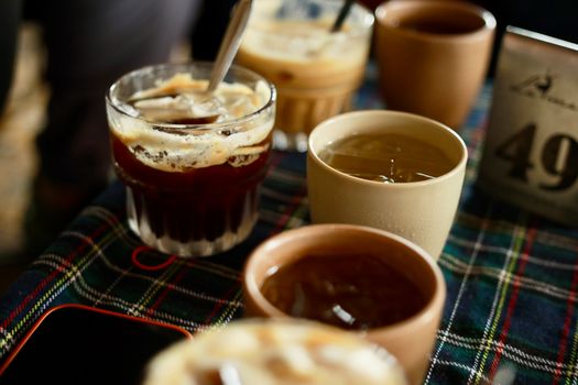 A variety of coffee drinks served in different cups on a plaid tablecloth, ready to enjoy.