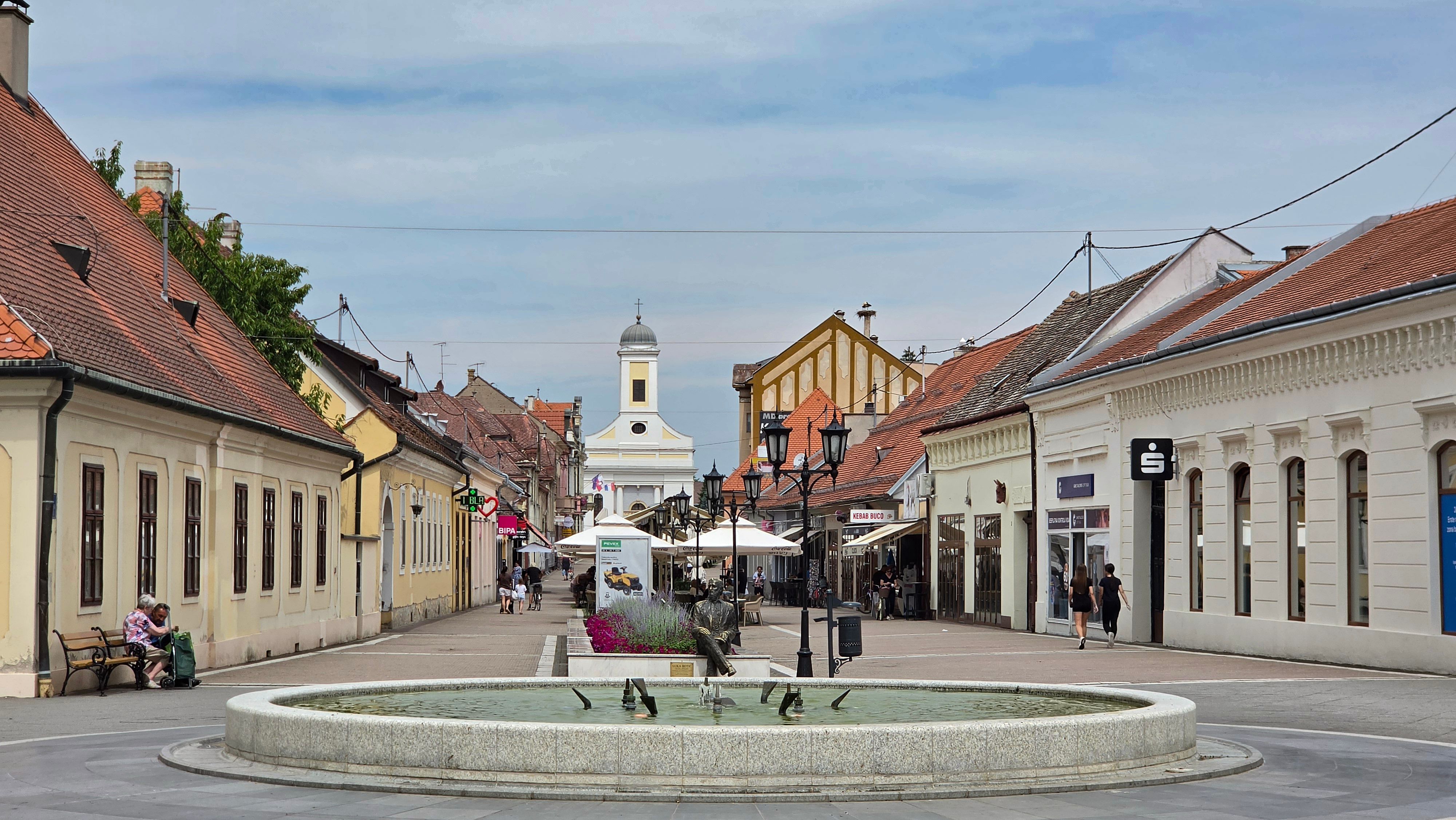 Picturesque walkway in a European town with a central fountain and historic architecture.