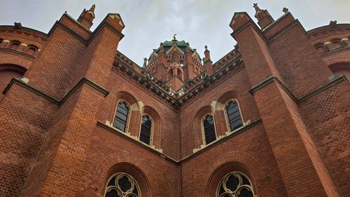 Free Dramatic view of a historic red brick cathedral with gothic architectural details and towering spires. Stock Photo