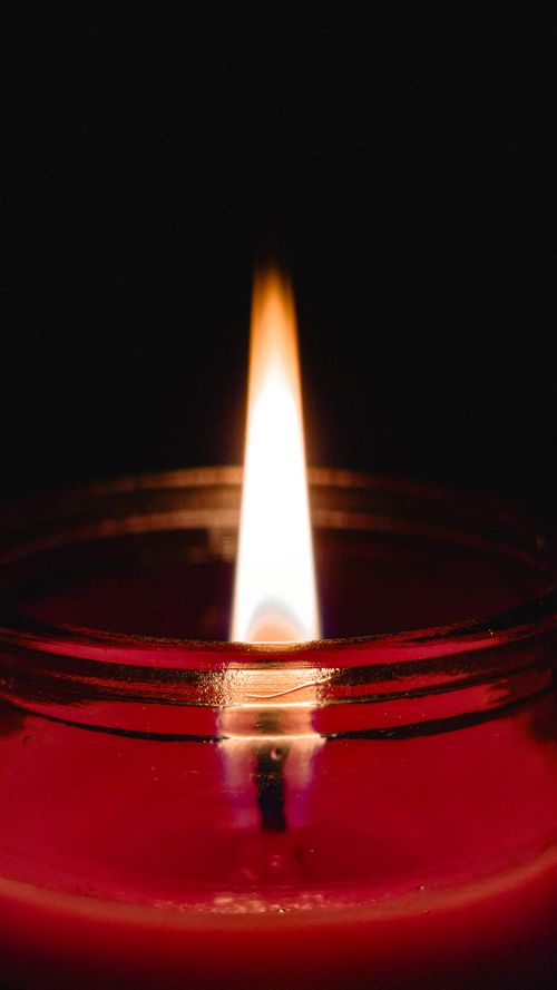 Free A close-up of a red candle with a glowing flame against a dark background. Stock Photo