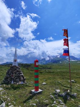 Stunning landscape of a mountain border marked by stones and flags under a vibrant sky.