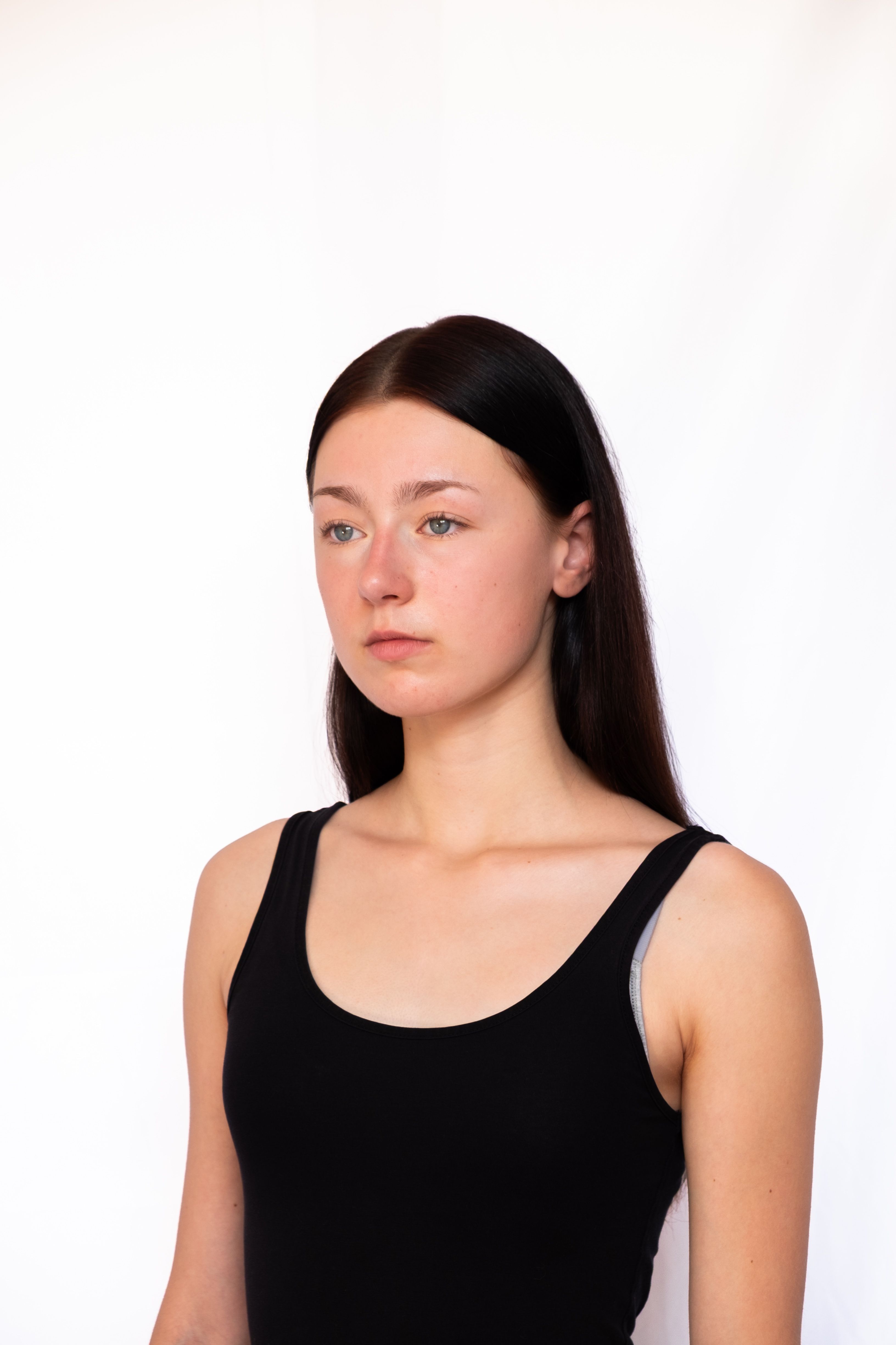 Elegant portrait of a young woman in a black tank top against a white background.