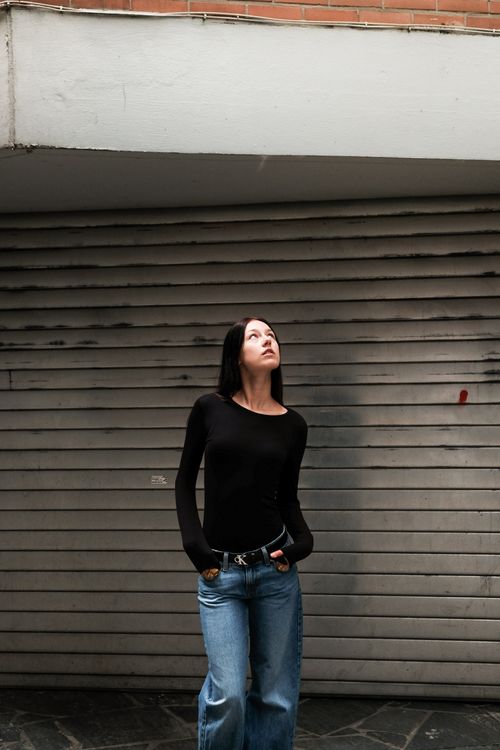 Free A young woman in casual attire looks up, standing beneath garage roofing in an urban setting. Stock Photo