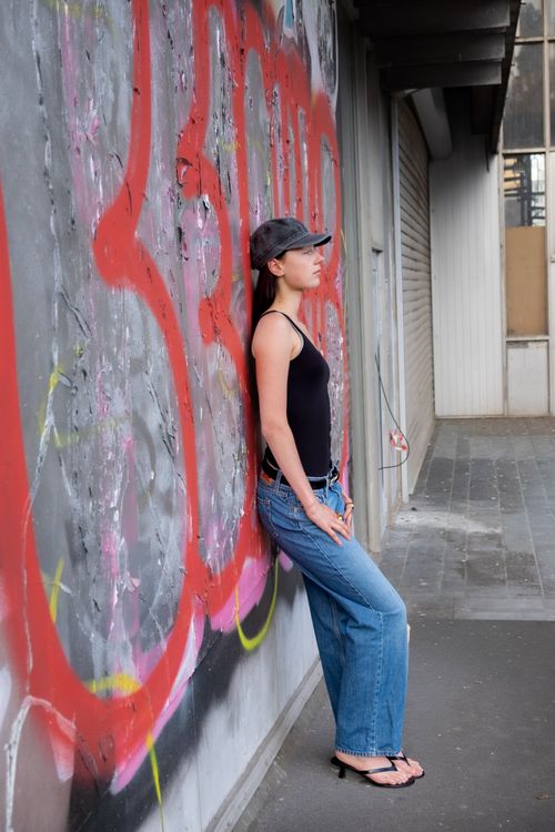 Free Woman in street attire poses by a colorful graffiti wall in an urban setting. Stock Photo