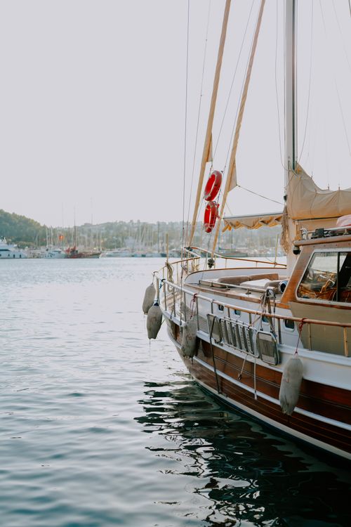 Free A classic yacht docked at Bodrum harbor during sunset, with a serene view of the Aegean Sea. Stock Photo