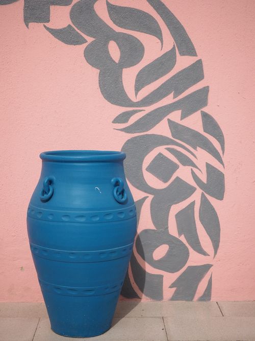 Free A vibrant blue vase stands against a pink wall adorned with gray artistic designs in Doha. Stock Photo