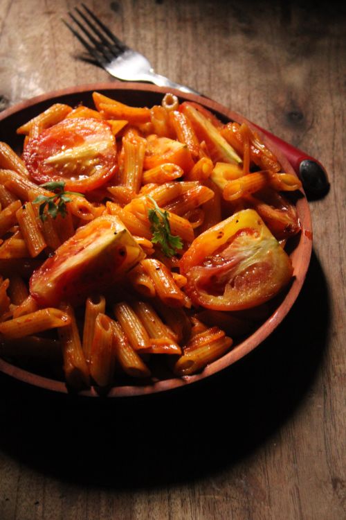 Free Savory penne pasta with fresh tomato slices, served on a rustic wooden table, perfect for gourmet food lovers. Stock Photo