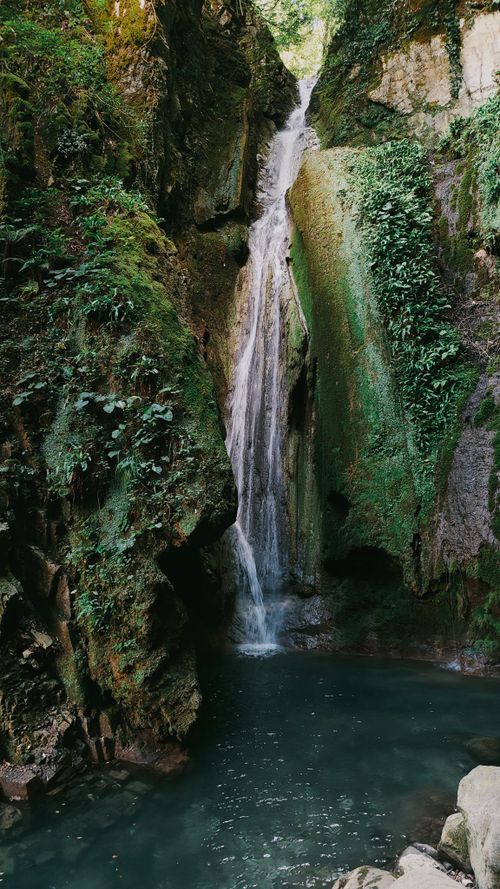 Free A tranquil waterfall cascades into a pool, surrounded by lush greenery and rocky terrain. Stock Photo