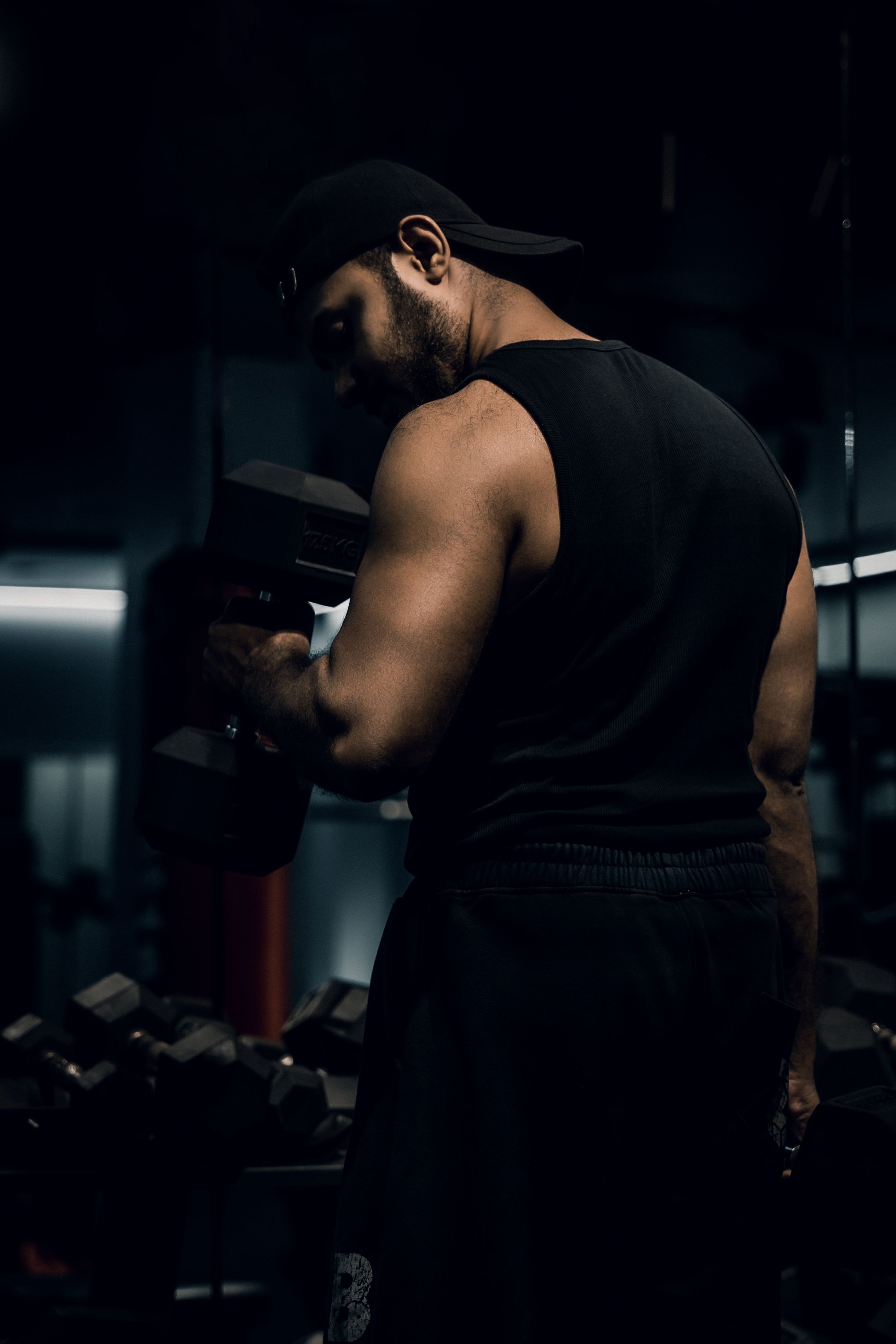 A muscular male athlete lifts dumbbells in a dimly lit gym, emphasizing strength and fitness.