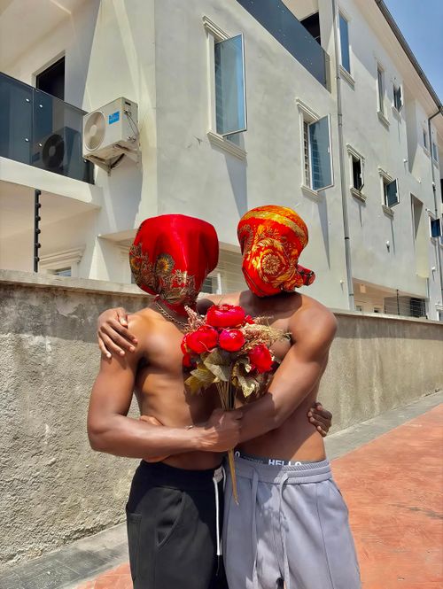 Free Two men with covered faces share an embrace while holding red flowers outdoors in Lagos, Nigeria. Stock Photo