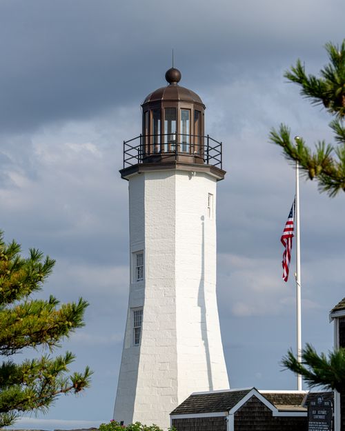 Free Scituate Lighthouse standing tall with an American flag under a cloudy sky. Stock Photo