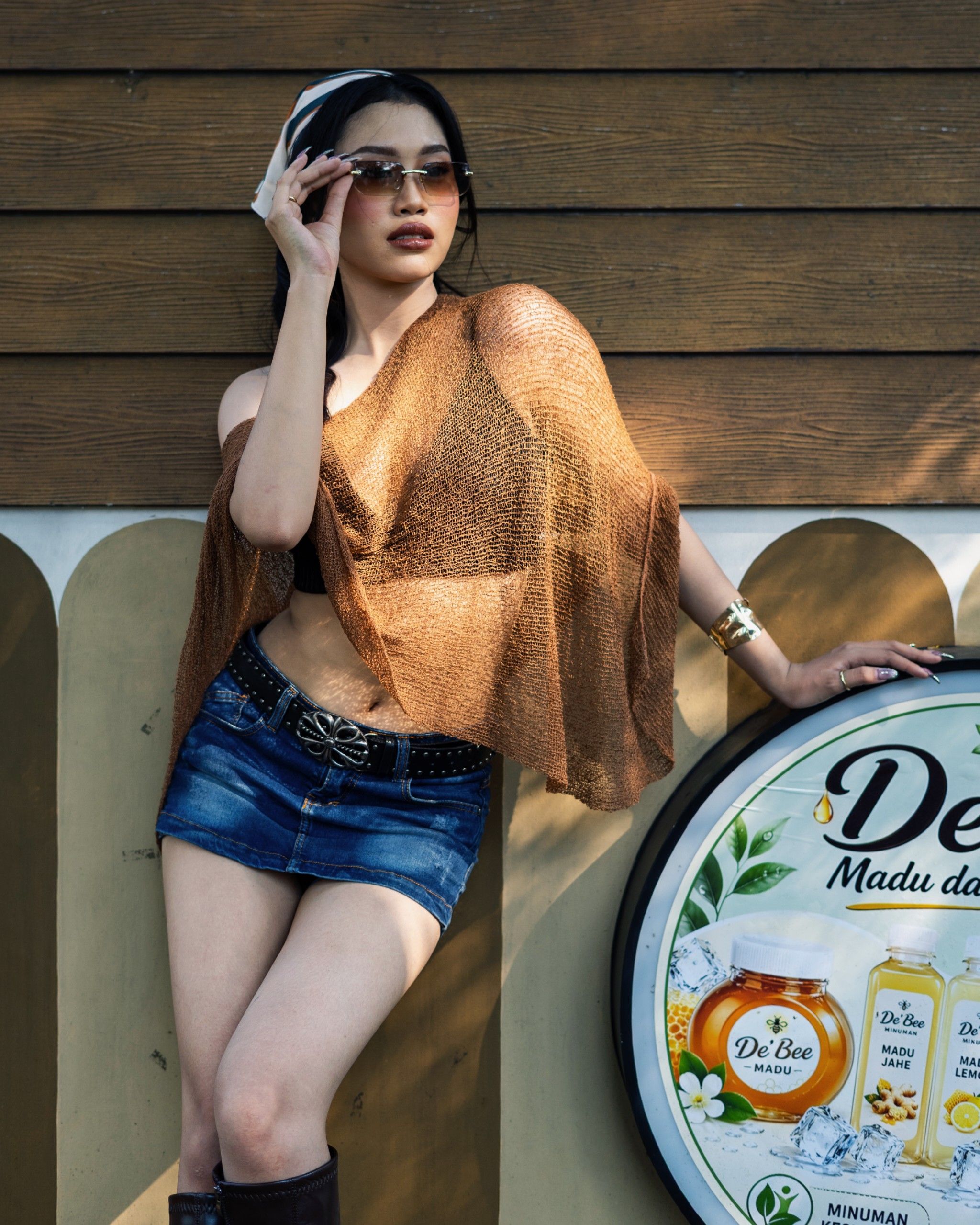 Fashionable woman with sunglasses poses stylishly outdoors against a vintage wall in Jakarta.
