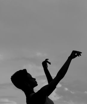 Silhouette of a graceful dancer in motion with arms raised against a dramatic cloudy sky.