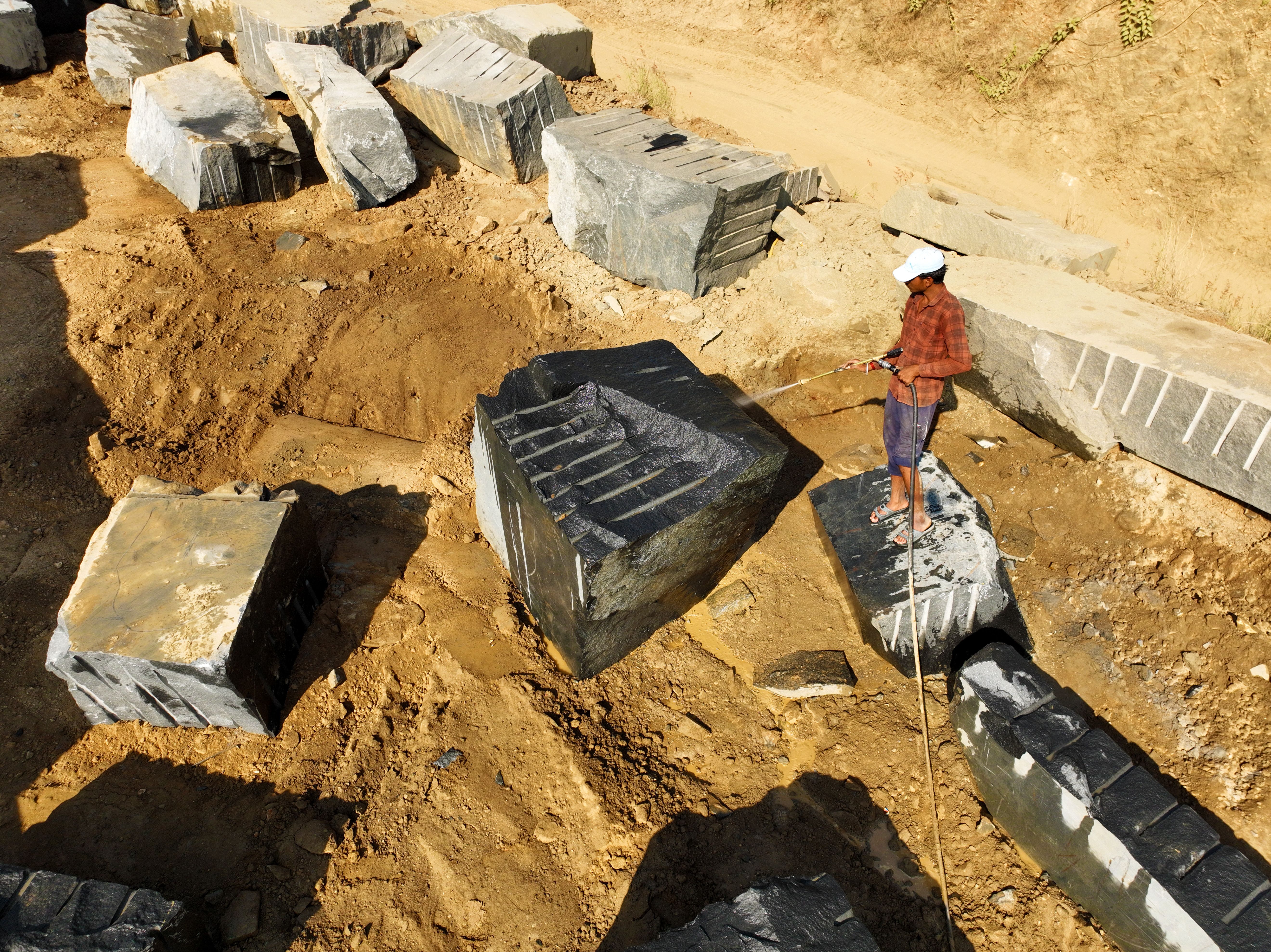 A worker operating at a granite quarry reveals large stone blocks and earth-moving activities.