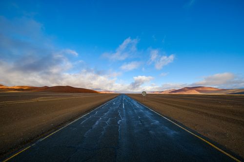 Free A scenic road stretches through the barren Namib Desert in Namibia under a vast blue sky. Stock Photo
